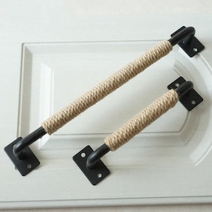 May include: Two black metal cabinet door pulls with a rope wrapped around the handle. The rope is a natural beige color.