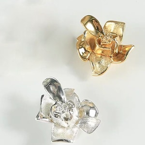 May include: Two flower-shaped charms, one gold and one silver, with a small clear stone in the centre of each.