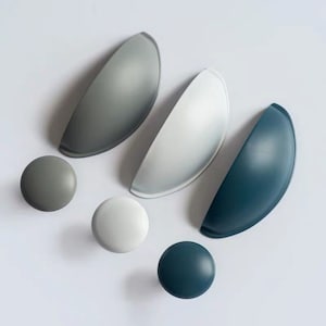Könnte beinhalten: Fünf Schrankknöpfe in verschiedenen Farben und Größen. Die Knöpfe sind aus einem glatten, festen Material gefertigt. Die Farben umfassen Grau, Weiß und Blau.
