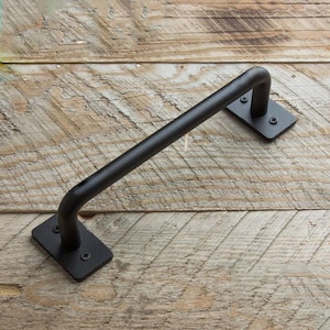May include: Black metal door handle with a curved design. The handle is mounted on a wooden surface.