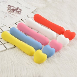 May include: A set of seven colorful silicone heart-shaped hair clips. The clips are in the colors red, white, pink, blue, light blue, yellow, and a light shade of yellow.