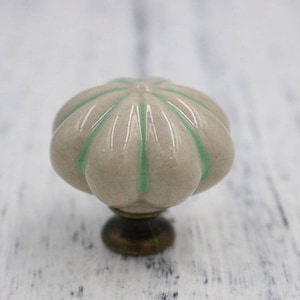 May include: A ceramic cabinet knob with a light grey base and green stripes. The knob has a rounded, slightly bulbous shape.