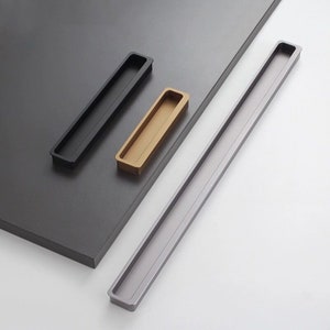 May include: Three cabinet pulls in different finishes: black, gold, and silver. The pulls are rectangular with a recessed centre.