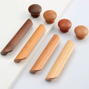 Peut inclure: Assortiment de boutons et de poignées de cabinet en bois dans différentes nuances de brun. Les boutons sont ronds et les poignées sont longues et rectangulaires.