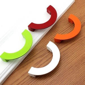 以下が含まれることがあります： 半円形の4つの異なる色のキャビネットプル。プルは赤、緑、オレンジ、白です。