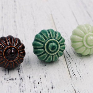 Pode incluir: Três botões de cerâmica com um design floral. Os botões são castanhos, verdes e verde claro.