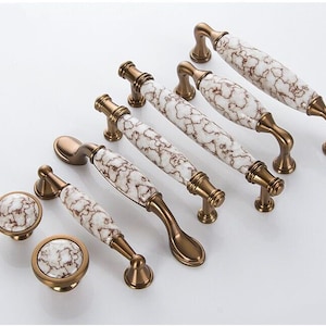 May include: Set of eight antique bronze cabinet knobs with white ceramic handles featuring a marbled design. The knobs are in various sizes and shapes.