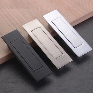 Op de afbeelding: Drie kastdeurgrepen in zwart, zilver en chroom. Elke greep heeft een rechthoekige vorm met een ingezonken handvat.