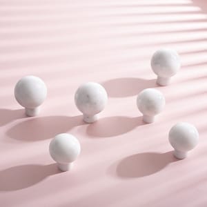 Może przedstawiać: Sześć okrągłych gałek meblowych z białego marmuru o gładkim, polerowanym wykończeniu. Gałki są ułożone na różowym tle.