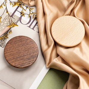 Peut inclure: Deux sous-verres ronds en bois, l'un brun et l'autre en bois clair, sur un fond blanc et vert.