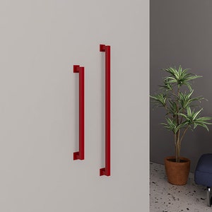 Pode incluir: Duas puxadores de porta de armário de metal vermelho, uma mais longa que a outra, montadas em uma parede branca.