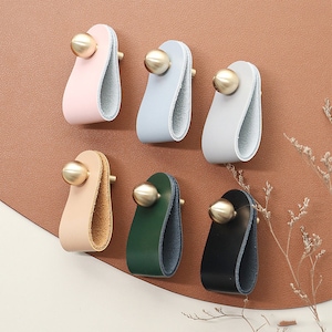 以下が含まれることがあります： 金色のノブが付いた革製のキャビネットプルが6つ。プルはピンク、ライトブルー、ベージュ、グリーン、ブラックなど、さまざまな色があります。