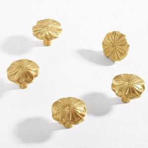 May include: Five gold-toned cabinet knobs with a floral design. Each knob has a raised centre and a scalloped edge.