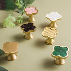 Peut inclure: Six boutons de porte en laiton avec des incrustations de différentes couleurs. Les boutons sont en forme de trèfle à quatre feuilles. Les incrustations sont noires, blanches, roses, vertes et dorées.