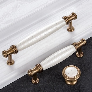 May include: Three cabinet knobs with a white ceramic finish and a brass base. The knobs have a geometric pattern on the ceramic surface.