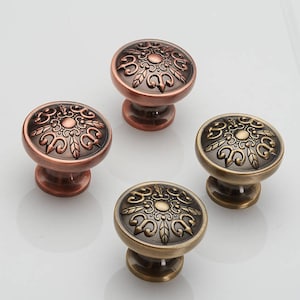 Könnte beinhalten: Vier verzierte Schrankknöpfe mit einem floralen Design. Zwei Knöpfe sind kupferfarben und zwei sind messingfarben.