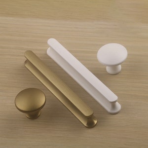 May include: Three cabinet pulls in two different styles. Two are rectangular bar pulls, one in gold and one in white. The other is a round knob in gold.