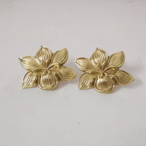 Op de afbeelding: Een paar gouden bloemvormige oorbellen. De oorbellen zijn gemaakt van metaal en hebben een gedetailleerd bloemmotief.
