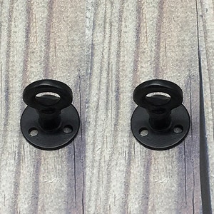 May include: Two black metal ring hooks with a round base and three screw holes. The hooks are mounted on a wooden surface.