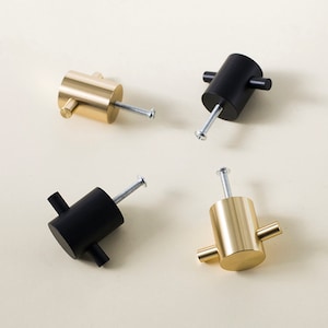 Peut inclure: Quatre boutons de meuble, deux noirs mats et deux en laiton brossé. Chaque bouton a un corps cylindrique avec deux petites barres horizontales s'étendant des côtés. Une vis est fixée pour l'installation.