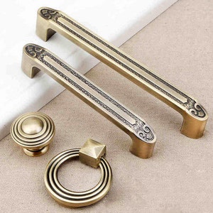 May include: Set of four antique gold-toned cabinet hardware pieces. Two drawer pulls with ornate designs and two decorative knobs.