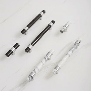 May include: Assortment of cabinet hardware pulls in black and white marble finishes. The pulls are made of metal and have a polished chrome finish.