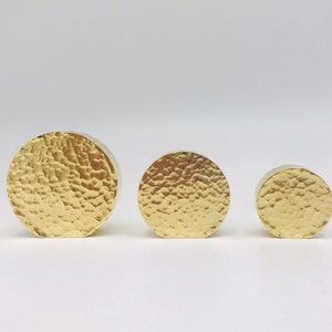 Könnte beinhalten: Drei runde, gehämmerte goldene Dekorationsobjekte in verschiedenen Größen.