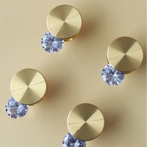 以下が含まれることがあります： 金色の丸いキャビネットノブが4つあり、それぞれに透明なクリスタル装飾が施されています。ノブは光沢のある研磨仕上げです。