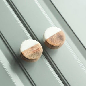 May include: Two round wooden knobs with a white half-circle on top. The knobs are on a grey surface.