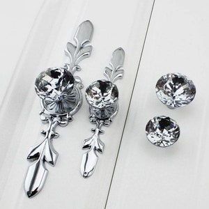 May include: Set of four silver cabinet knobs with crystal accents. The knobs feature a decorative design and are perfect for adding a touch of elegance to any room.