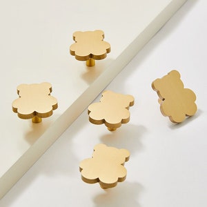 Op de afbeelding: Goudkleurige kastknoppen in de vorm van teddyberen. De knoppen zijn gemaakt van massief messing en zijn gerangschikt op een wit oppervlak. De knoppen hebben een matte afwerking en een eenvoudig ontwerp.