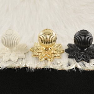 Op de afbeelding: Drie decoratieve kastknoppen met een bloemmotief. De knoppen zijn in wit, goud en zwart.