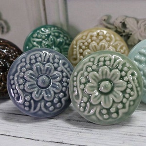 May include: Six ceramic knobs with a floral design in various shades of blue and green. The knobs are round and have a raised, embossed flower pattern.