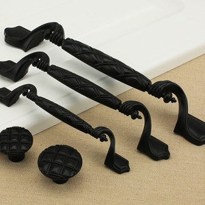 May include: Four black metal cabinet knobs with a square, quilted design. The knobs are in various sizes and have a decorative, ornate finish.