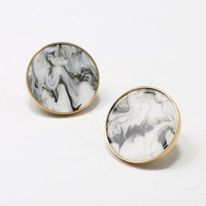 May include: Two round, white marble cabinet knobs with a gold metal rim. The marble has a black and white swirl pattern.