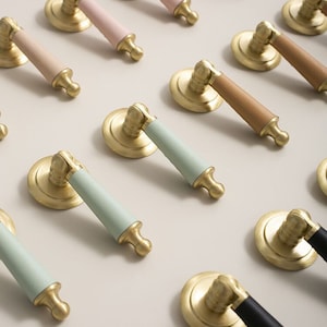 Peut inclure: Une collection de poignées de porte de placard décoratives avec des lanières de cuir de différentes couleurs. Les poignées sont en métal doré et ont une base ronde. Les lanières de cuir sont dans des tons de rose, vert clair, marron et noir.