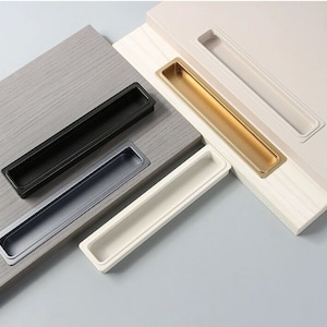Puede incluir: Cuatro tiradores de cajón de armario en varios acabados. Los tiradores son de metal y tienen una forma rectangular con un centro empotrado. Los acabados incluyen negro, dorado, plateado y blanco.