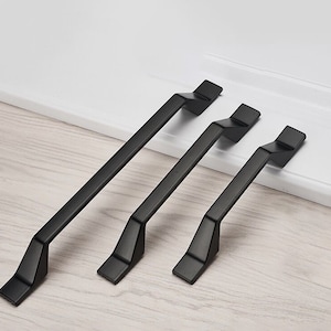 Peut inclure: Trois poignées de tiroir en métal noir de différentes tailles. Les poignées ont un design moderne et géométrique avec une forme rectangulaire et des bords angulaires.