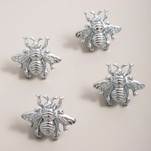 Op de afbeelding: Vier zilveren trekknoppen in de vorm van een bij. De bijen hebben gedetailleerde vleugels en lichamen.