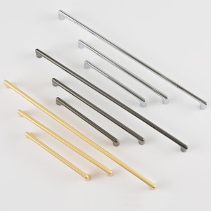 May include: Assortment of cabinet hardware pulls in three finishes: silver, gold, and dark gray. The pulls are all straight and have rounded ends.