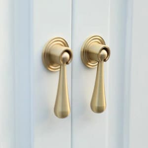 Op de afbeelding: Twee goudkleurige deurgrepen met een traanvorm. De grepen zijn gemonteerd op een witte deur.