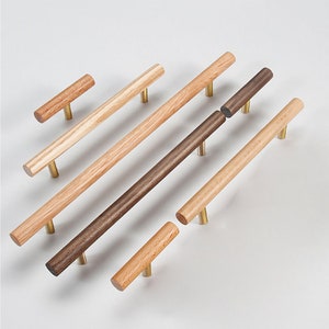 Könnte beinhalten: Sortiment an Holz-Schrank-Knöpfen und Schubladen-Griffen mit Messingbeschlägen. Die Knöpfe sind kurz und die Griffe sind lang. Das Holz ist hellbraun und dunkelbraun.