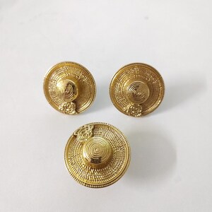 Op de afbeelding: Drie gouden oorbellen in de vorm van strohoeden met een bloemdetail.