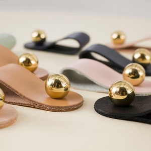 May include: A set of leather drawer pulls with gold metal knobs. The pulls come in a variety of colours, including black, brown, pink, and white.