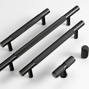 Peut inclure: Ensemble de quincaillerie de meubles noire, comprenant plusieurs poignées de tirage et deux boutons. Les poignées ont une prise texturée en forme de losange et sont montées sur une surface blanche. Idéal pour les armoires et les tiroirs.