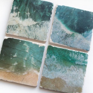 Op de afbeelding: Set van vier vierkante onderzetters met een strandscene. De onderzetters tonen een blauwgroene oceaan met witte schuimende golven en een zandstrand.