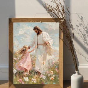 May include: A framed print depicts a figure in white robes with a child in a pink dress in a field of flowers. The artwork has a soft, painterly style with a light color palette. The frame is made of light brown wood.
