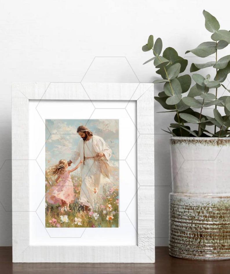 May include: A framed print depicts a figure in white robes with a child in a pink dress, set in a field of flowers. The artwork has a soft, painterly style, with a white wooden frame. A potted plant is visible on the right.