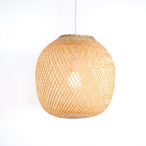 Op de afbeelding: Een ronde, natuurlijke geweven bamboe hanglamp met een wit snoer.