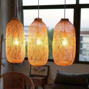 Könnte beinhalten: Drei Hängeleuchten mit gewebten Rattanschirmen beleuchten ein Wohnzimmer. Die zylindrischen Schirme haben eine warme, natürliche Farbe. Der Raum verfügt über einen Holztisch, einen Korbstuhl und ein dunkel gefärbtes Sofa.